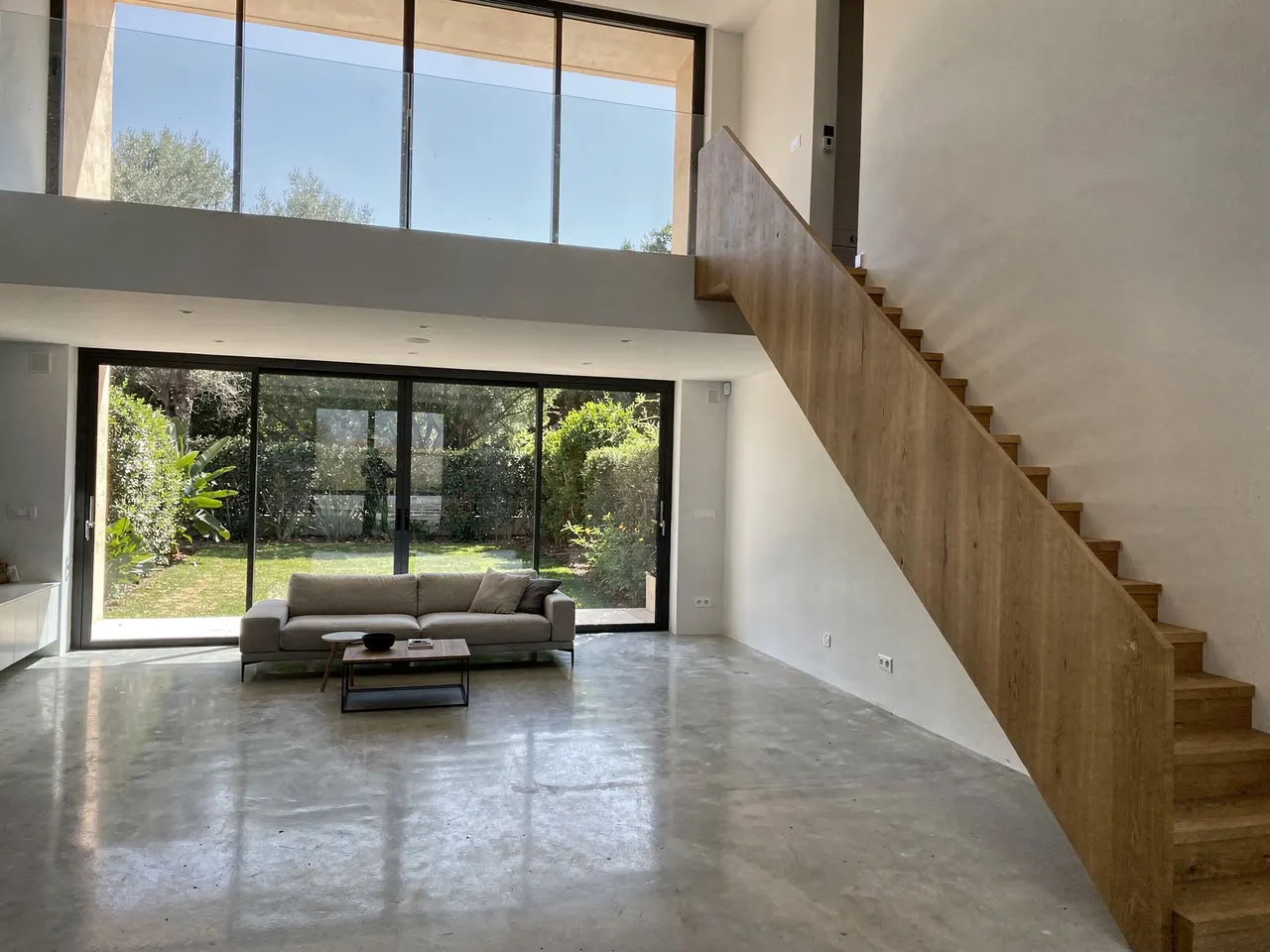 Salón a doble altura con escalera de madera y ventanal al jardín